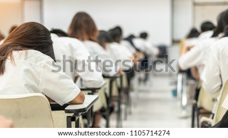 School student exam in university class with blurry view from back of the classroom of young people having stress doing examination admission test in classroom for education background