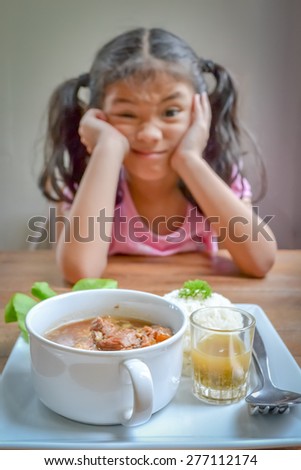 Little girl getting bored of food in blurred background (focus on cup of food) : Asian kid refusing to have a meal with negative expression