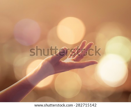Human hand reaching upward in midst of glowing gold candle lights bokeh, candlemas: Female woman empty open hand, palm praying in warm color tone background: Pray for peace: Sunday advent: Holy spirit