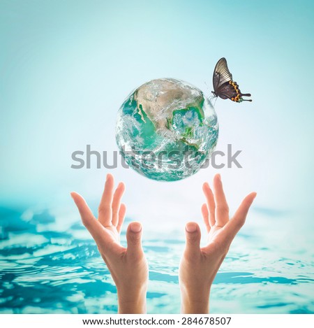 Green planet with butterfly above human hands on turquoise blue water background : World ocean and environment concept: Healthy oceans, healthy planet : Elements of this image furnished by NASA