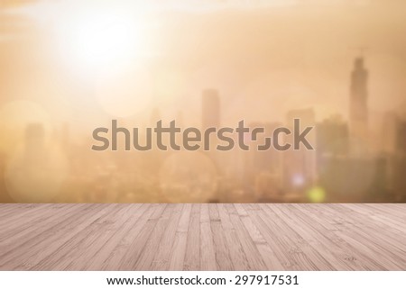 Aerial view of blurred abstract background of morning sunrise with flare from the kitchen balcony with wood floor in red brown color tone: Wooden table with blur cityscape view with gold light