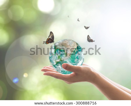 Hands holding green planet with butterflies on blurred green color bokeh background of natural tree leaves facing sun flare: Saving world environment concept: Elements of this image furnished by NASA