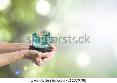 Human hands holding green globe on perfect soil with blurred greenery bokeh background of tree leaves with sunlight (focus on soil): World environment concept: Elements of this image furnished by NASA