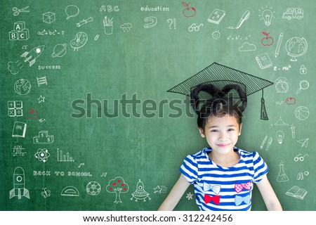 Happy Asian school child girl with big graduation cap/ hat on green color chalkboard background with freehand daydreaming doodle and blank copy space: Smiling female little kid on writable blackboard