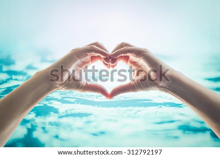 Human happy hands in heart shape showing love and friendship on blurred wavy clean blue turquoise color water background: Saving world water and natural environment and ocean concept/ campaign/ idea
