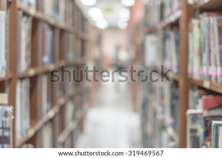 Blurred abstract background of a view an aisle of book shelves in school library: Blurry interior perspective of a study room with tables, chairs and stacks of books