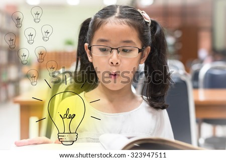 Surprising creative idea lighttbulb pop up from book in front of little asian child girl with eyeglasses (Selective focus): Student kid reading book in library looking at light bulb with excitement