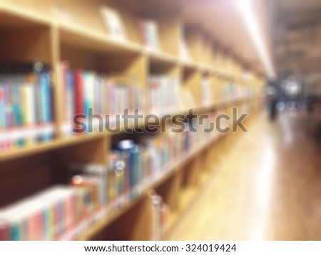 Blurred abstract background of public library interior with aisle of bookshelf with textbooks and furniture for reading area: Blurry perspective view of educational study room space with book shelves