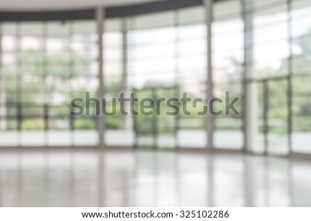 Blurred abstract background interior view looking out toward to empty office lobby and entrance doors/ glass curtain wall with frame: Blurry perspective of reception hall to public building entrance