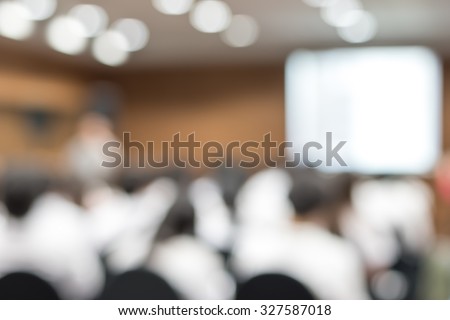 Blurred abstract background of university students sitting in a lecture room with teacher in front of the class with white projector slide screen: Blurry view from back of the classroom: Teachers day