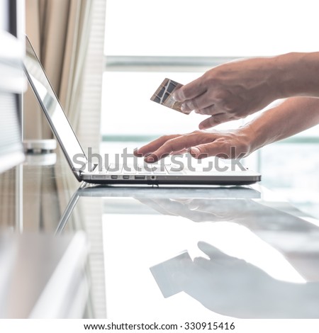 Human woman hand holding credit card while using computer for internet product ordering/ online shopping (Selective focus): Female buyer/ customer typing credit card number order goods from home