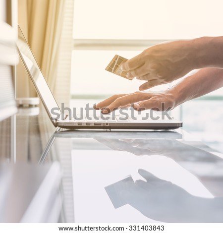 Human woman hand holding credit card while using computer for internet product ordering/ online shopping (Selective focus): Female buyer/ customer typing credit card number order goods from home