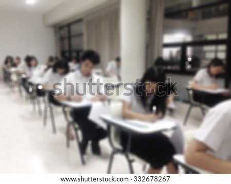 Blurred abstract background of group of asian students having mid-term examination in school: Blurry view  inside class of university/ college students sitting in rows doing final exam in classroom