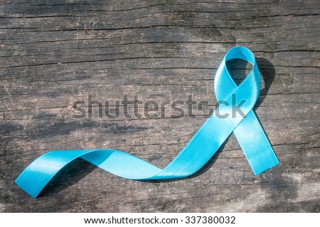 Light blue ribbon symbolic sign for prostate cancer awareness campaign and men\'s health in November on grunge old hardwood/ wood background: Shiny blue satin texture textile on dark wooden backdrop