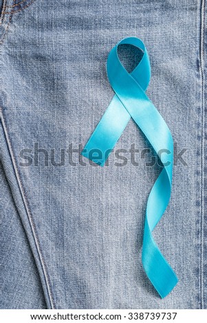Light blue ribbon symbolic sign for prostate cancer awareness campaign/ concept and men\'s health promotion in November on Jeans denim background: Shiny blue ribbon texture textile on Jeans backdrop