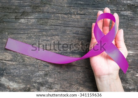 Purple color ribbon in women\'s human hand on grunge old aged wood background symbolic logo concept raising awareness on Alzheimer\'s disease, Breastfeeding, Eating disorder, November caregivers month