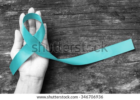 Teal ribbon awareness to support Cervical Cancer on black and white human hand with wood background: Symbolic concept for raising awareness/ concerns/ help and campaign on people living with illness