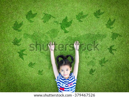 Happy Asian girl child raising hands w/ happiness lying peacefully w/ dove birds sign in heart shape on natural eco bio green grass: Peaceful mind kid in beautiful clean park environment: CSR concept