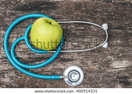 Green fresh organic natural nutrient apple with doctor's stethoscope heart shape on grunge old aged wood background: World health day WHD April 7 symbolic conceptual design idea for healthy fruit food