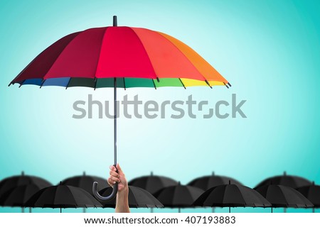 Leader person's hand holding rainbow umbrella distinctive unique among black color others on blue mint vintage sky background: Life-health Insurance protection, Business financial leadership concept