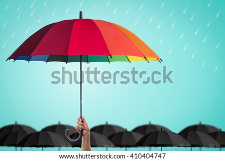 Leader person\'s hand holding rainbow umbrella distinctive unique among black color others on blue mint rainy sky background: Life health Insurance protection, Business financial leadership concept