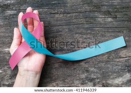 Pink blue ribbon on human helping hand on old aged wood background: Fabric symbolic color logo icon concept for raising awareness concerns support help campaign people with SID Birth defects illness