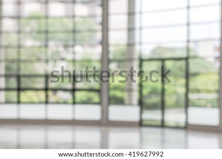 Blurred abstract background interior view looking out toward empty vacant office lobby and entrance doors and glass curtain wall frame: Blurry perspective of reception hall to building main entrance