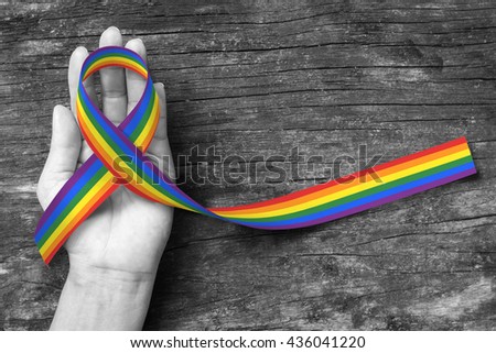 Rainbow color ribbon awareness on human hand on BNW background + clipping path:  Symbolic color logo icon for equal rights in love and marriage social equality of LGBT community/ people concept