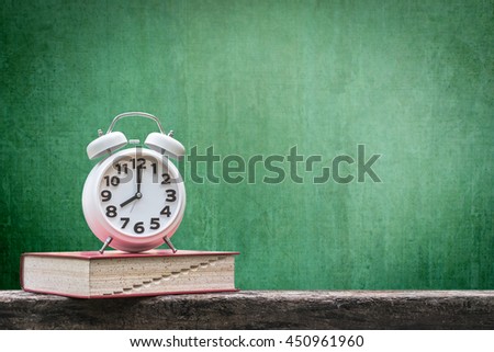 Back to school: Green chalkboard background for announcement w/ wake up alarm clock & textbook on grunge old dark wood table top+ copyspace: Students\' educational time for learning system concept