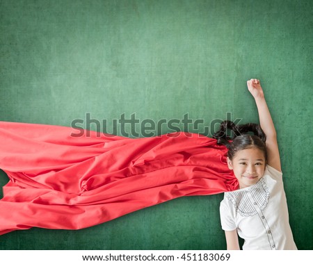 Happy healthy superhero strong powerful little Asian school student girl kid with red scarf dress costume in flying pose on grunge green chalkboard background: Girl power super woman education concept