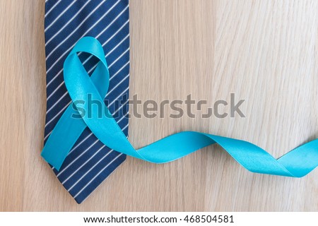 Light blue ribbon symbolic sign for prostate cancer awareness campaign and men\'s health in November and September on necktie & wood background: Shiny blue satin texture textile on wooden backdrop