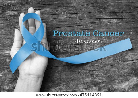 Light blue ribbon on helping hand support, wood background (clipping path) Symbolic sign for prostate cancer awareness, men\'s health campaign in November, September: Shiny blue fabric texture logo