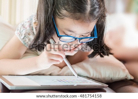 Happy Asian girl kid with blue light protection len eyeglasses enjoy using pen on tablet smart technology gadget pc device drawing doodle: Little school child draw cartoon pro innovative touchscreen