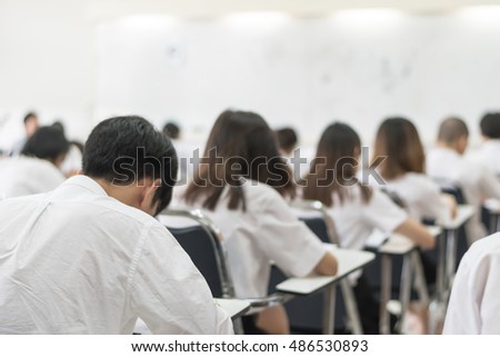 Blurred abstract background of university students in uniform attending examination in a classroom in educational institute: Blurry rear view of college people having exams in class room in seat rows