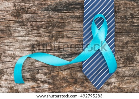 Light blue ribbon symbolic sign for prostate cancer awareness campaign and men\'s health in November and September on necktie on grunge wood table background: Shiny blue satin on wooden backdrop