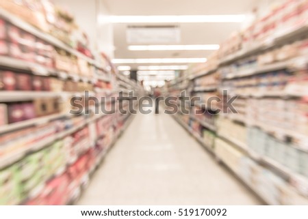 Blurred abstract background inside grocery store/ supermarket with shelves of many food products and diary supplies: Blurry perspective view of indoor space of market / food retail shop interior