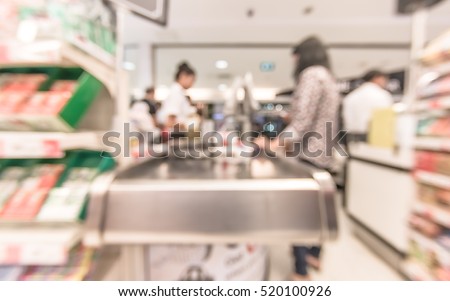 Blurred abstract background at cashier checkout payment counter inside grocery store with  buyer, shelves of products and supplies: Blurry perspective view indoor space of market / food shop interior
