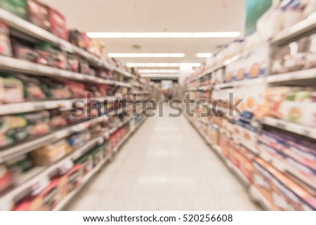 Blurred abstract background inside grocery store/ supermarket with shelves of many food products and diary supplies: Blurry perspective view of indoor space of market / food retail shop interior