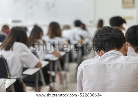 Blurred background university students in uniform attending doing examination in educational school classroom: Blurry rear view college people sit in class room seat rows having exams writing answer