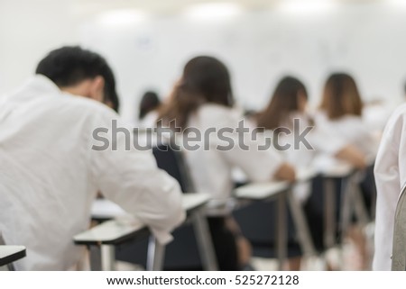 Blurred abstract background of university students in uniform attending examination in a classroom in educational institute: Blurry rear view of college people having exams in class room in seat rows