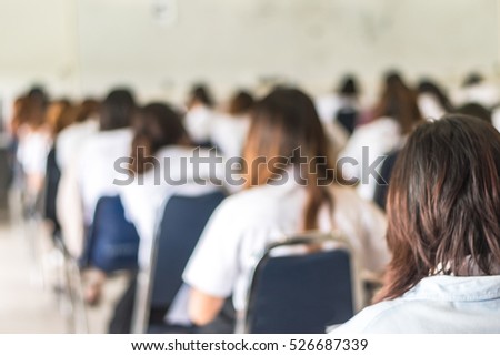 Blurred abstract background university students in uniform attending examination a classroom educational institute: Blurry rear view of college people having exams in class room seat rows