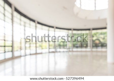 Blurred abstract background interior view looking out toward to empty office lobby and entrance doors and glass curtain wall with frame: Blurry perspective of reception hall to building entry/ exit