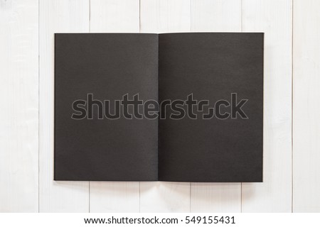 Blank A4 size black book template with open double page placing on creamy white surface wood background flat lay: Empty paperback magazine catalog note book paper texture mockup on wood table backdrop