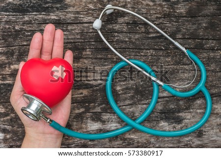 Red heart love shape with cross bandage on woman's hand and medical doctor physician's stethoscope on old aged wood for hospital healthcare insurance business and world health day concept