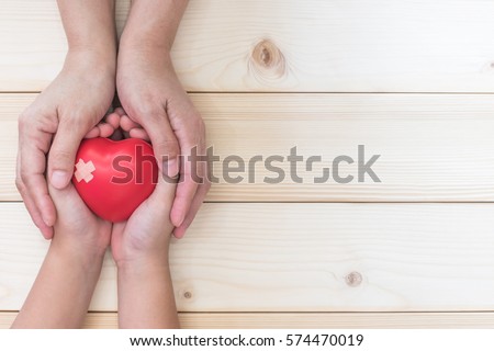 Mom mother\'s hand holding daughter son child kid palm support red heart love ball, bandage, light white wood background: Nursing children home day care health care concept: Hospital medical business