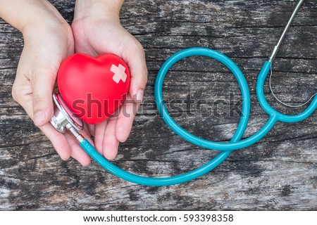Healthcare medical insurance business and world heart health day concept with red heart and bandage (band-aid) on woman\'s hands support with doctor\'s stethoscope
