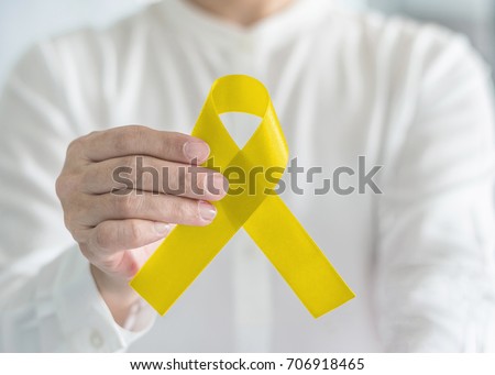 Yellow ribbon symbolic bow color for suicide prevention, sarcoma bone cancer and spina bifida awareness month in supporter person\'s hand