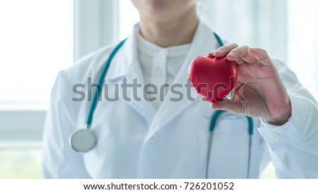 Cardiovascular disease doctor or cardiologist holding red heart in clinic or hospital exam room office for professional medical, csr cardiology health care service and world heart health day concept