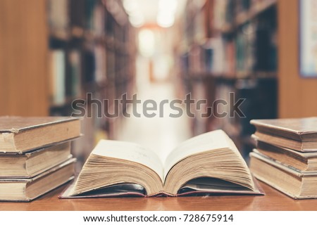 Old book in library with open textbook, stack piles of literature text archive on reading desk, and blur aisle of bookshelves in school study class room background for education learning concept