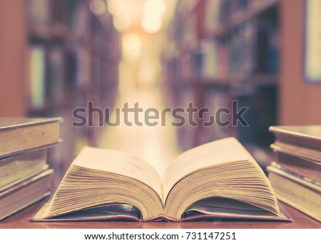 Old book in library with open textbook, stack piles of literature text archive on reading desk, and blur aisle of bookshelves in school study class room background for education learning concept